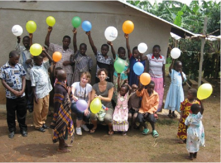 Menschen vor einem Gebäude in Uganda winken und halten bunte Luftballons in die Höhe