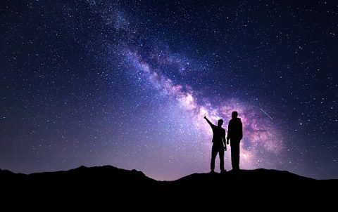 Milky Way with silhouette of a family on the mountain. Father and a son who pointing finger in night starry sky. Night landscape. Beautiful Universe. Space. Travel background with sky full of stars