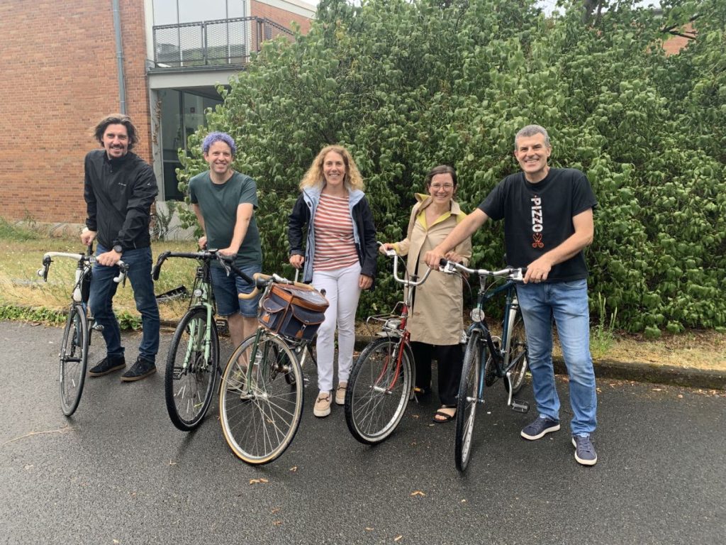 Das Bild zeigt fünf Mitglieder des Fahrradteams des Sprachenzentrums. Sie stehen nebeneinander auf einem Parkplatz und halten ihre Fahrräder fest.