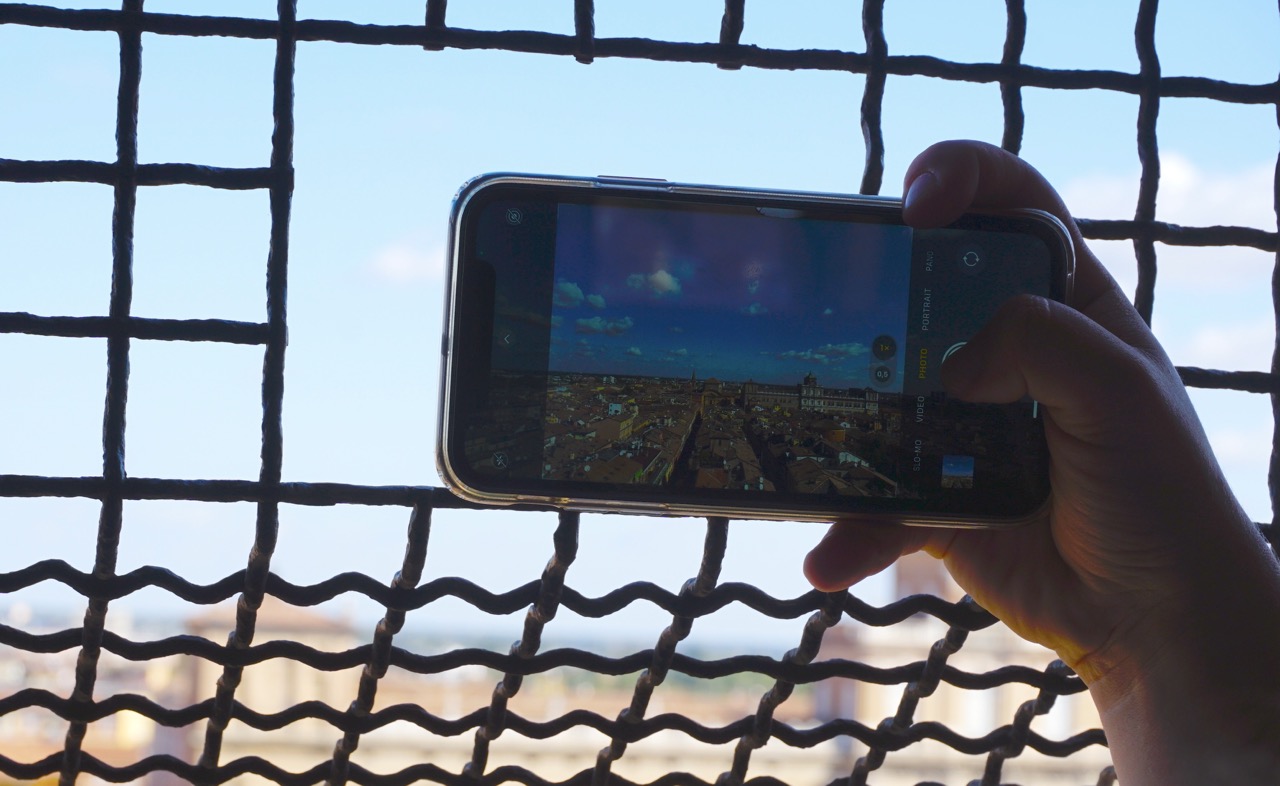 Handy fotografiert Stadtansicht von Modena durch ein Schutzgitter; Nahaufnahme.