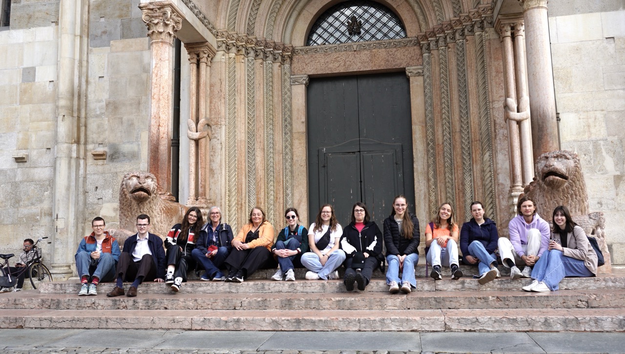 Gruppe sitzt auf den Domstufen von Modena vor Löwenfiguren.