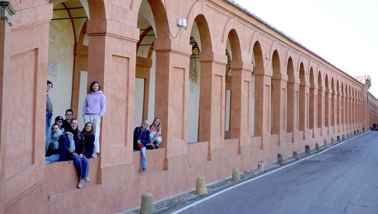 Teilnehmende sitzen in Nischen der langen Arkaden zur San Luca-Basilika.