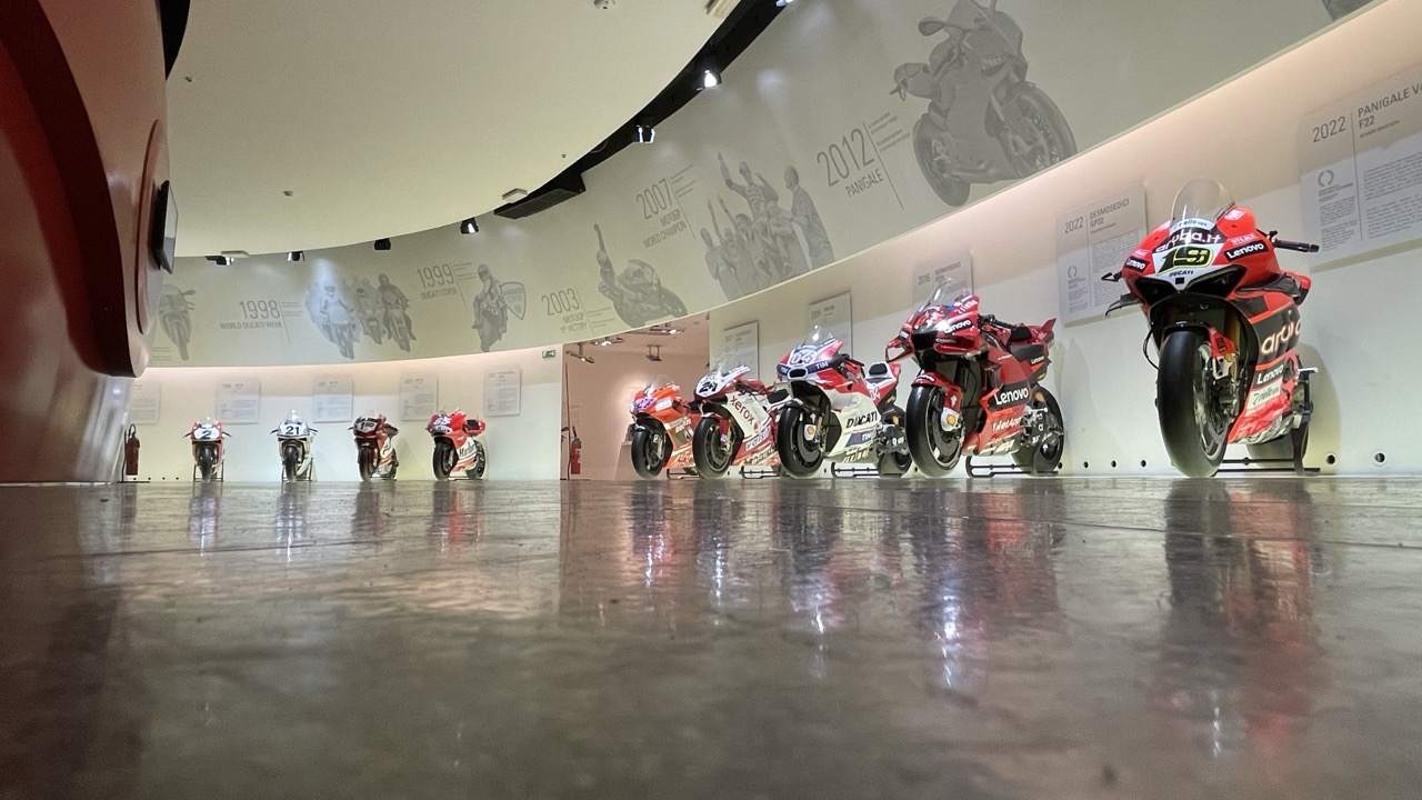 Reihe von Ducati-Rennmotorrädern im Museumsraum mit Zeitstrahl an der Wand.