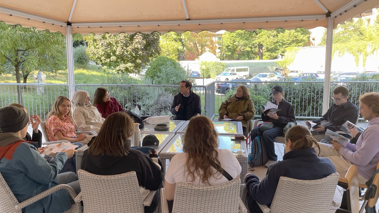 Rundgespräch im Freien unter Markise; Teilnehmende mit Heften.