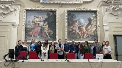 Gruppenfoto in prunkvollem Saal mit zwei großen Wandgemälden.